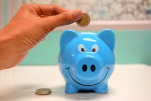 A blue piggy bank with a hand preparing to drop a coin into the top.