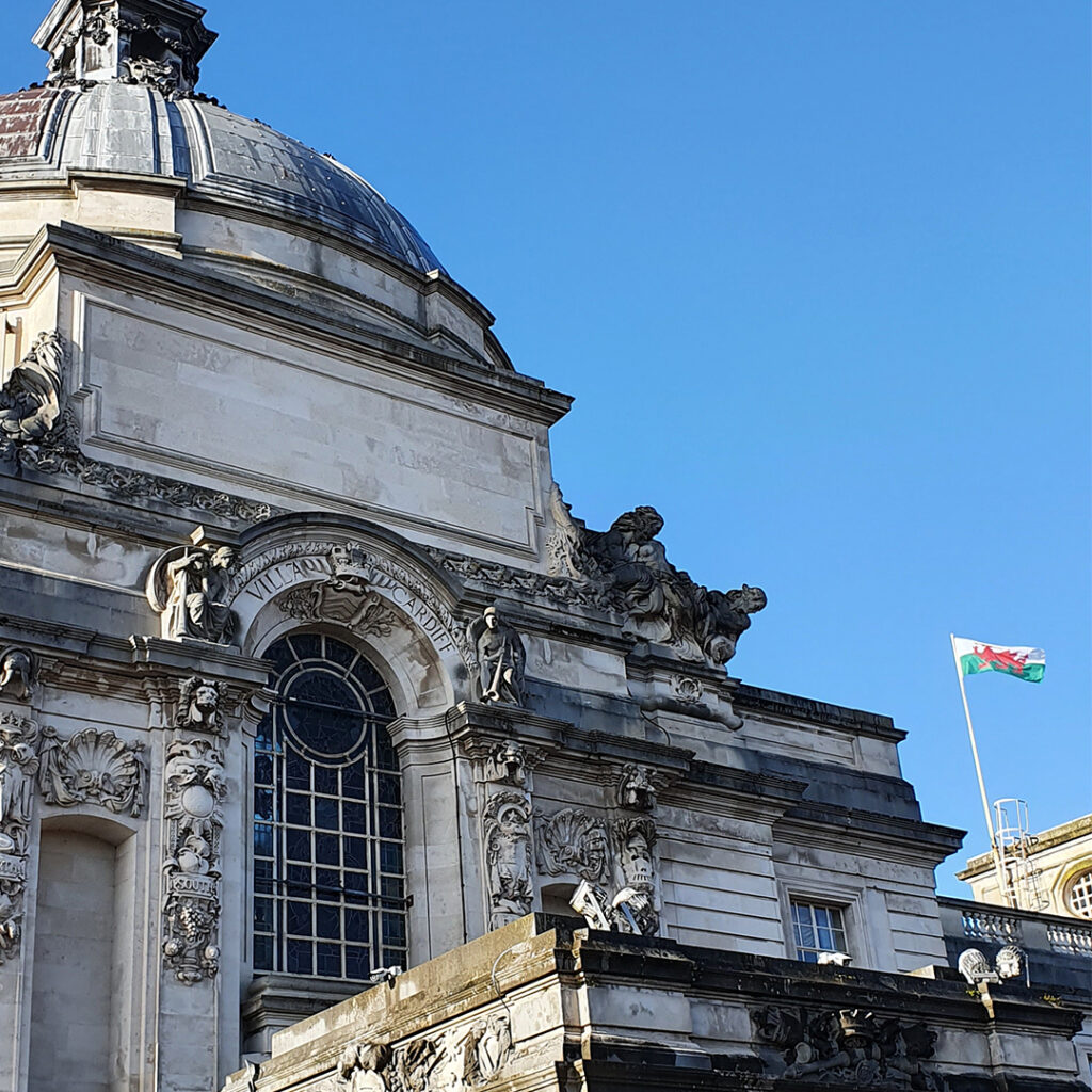 A view of Cardiff City Hall against a blue sky. The welsh flag is visible on the right.