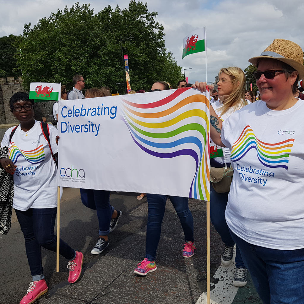 People marching in a parade holding a banner depicting a rainbow and 'Celebrating Diversity' written