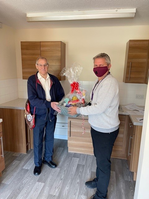 Mr Condron is handed a hamper with gifts in by a member of CCHA staff. Both are stood in a brand new kitchen, smiling at the camera.