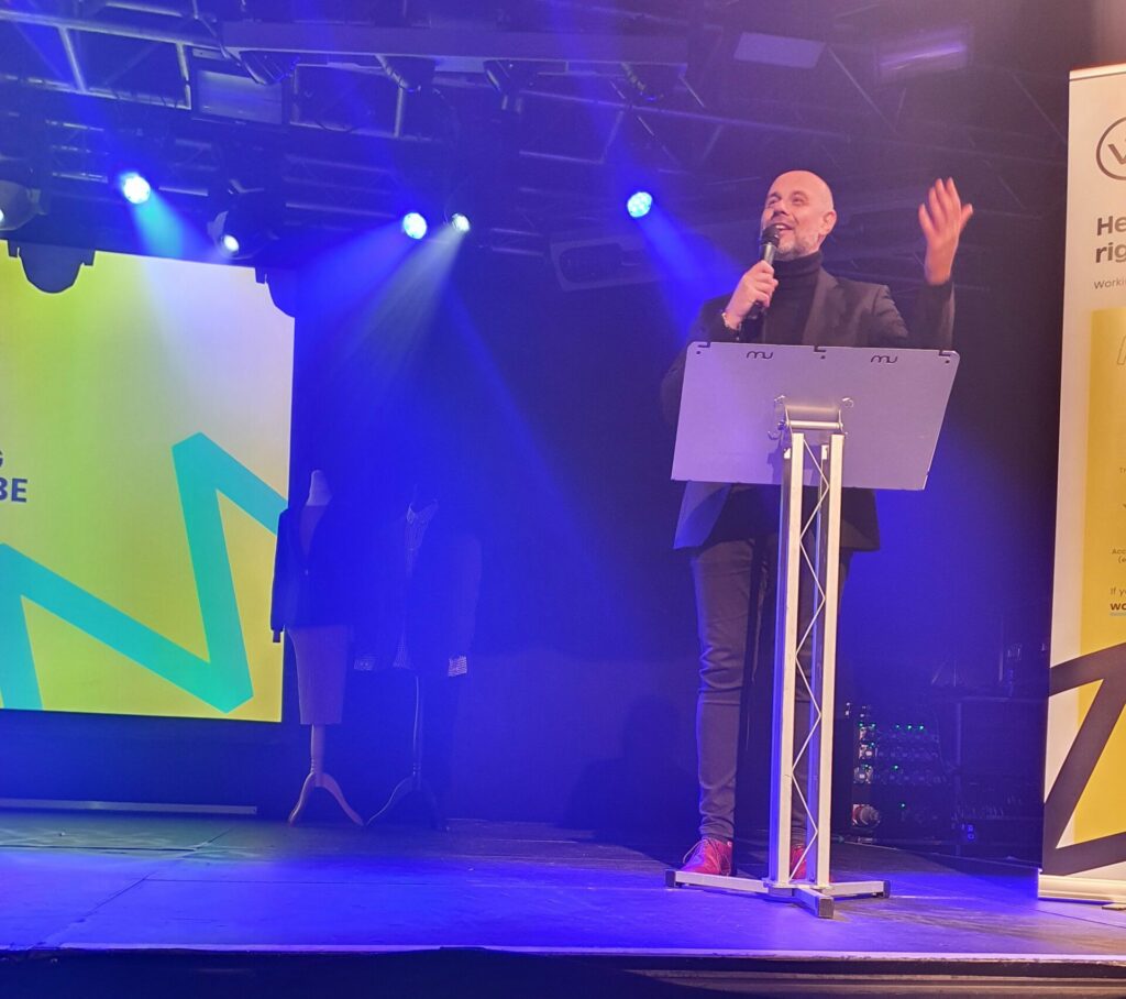 Jason Mohammad stands at the lectern and speaks into a microphone