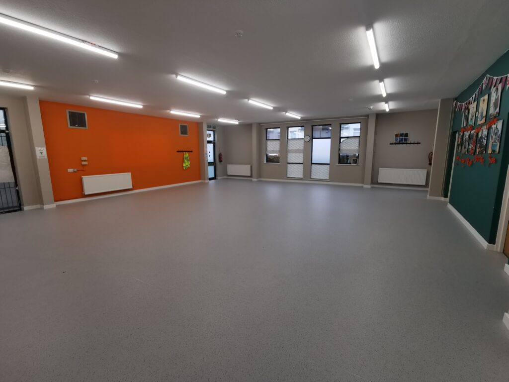A hall with a window at the far end of the room, an orange wall on the left, and a green wall on the right